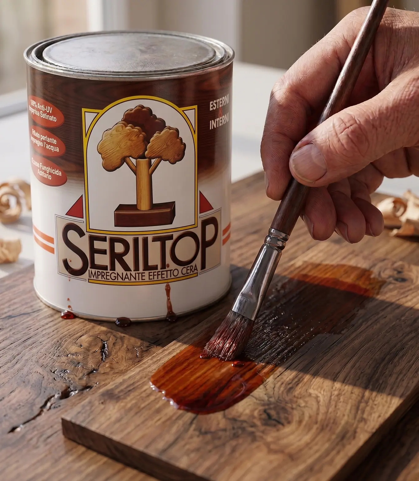 Die Dose Seriltop, Imprägnierung mit Wachseffekt, daneben eine Hand, die das Produkt mit dem Pinsel auf ein dunkles Brett aufträgt