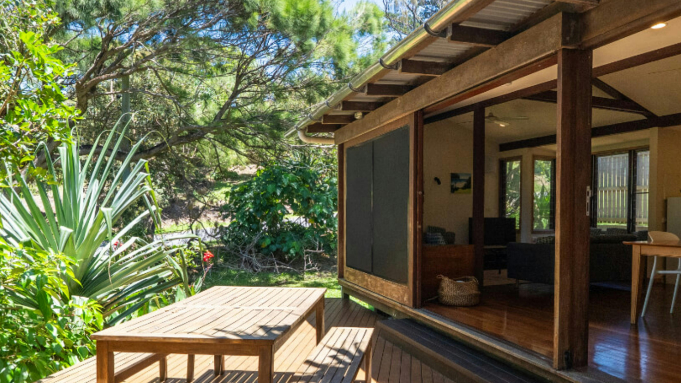 Tisch und Bänke aus Holz auf einer Holzterrasse unter der Veranda eines Hauses