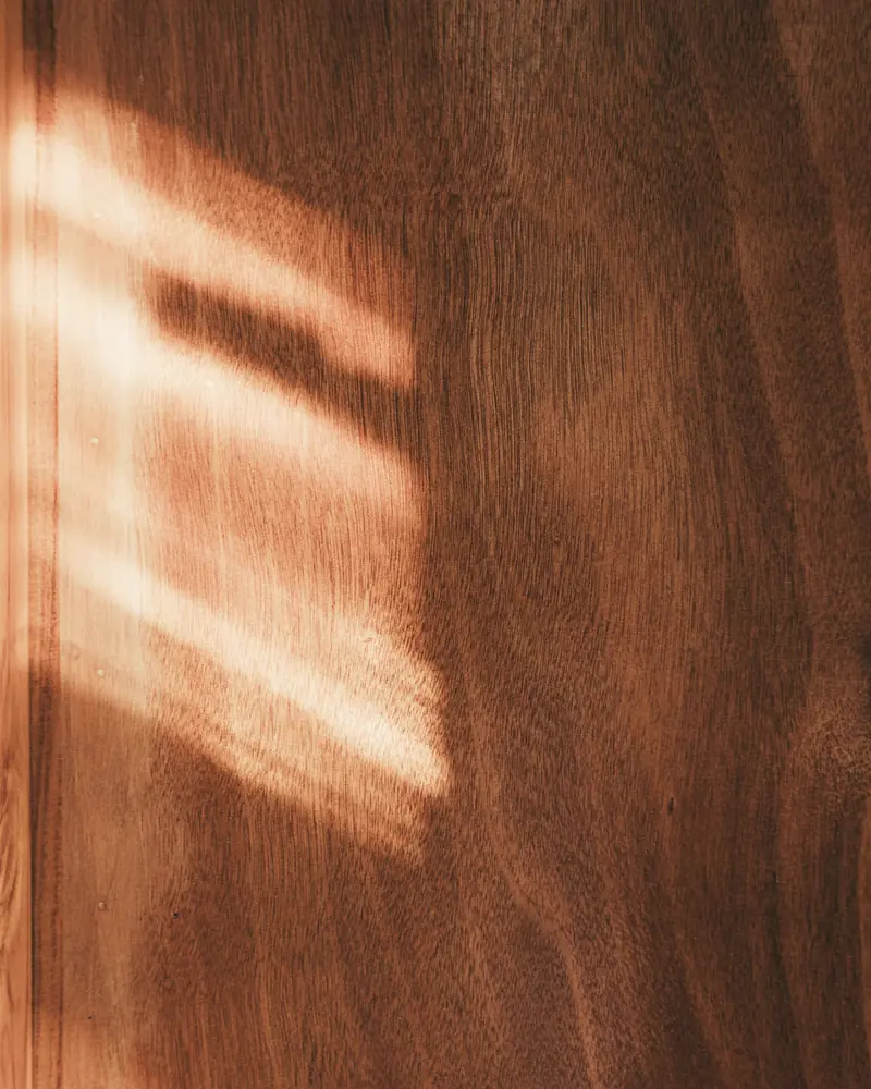 Primo piano di un pannello in legno con venature verticali illuminato di lato da una lama di luce calda