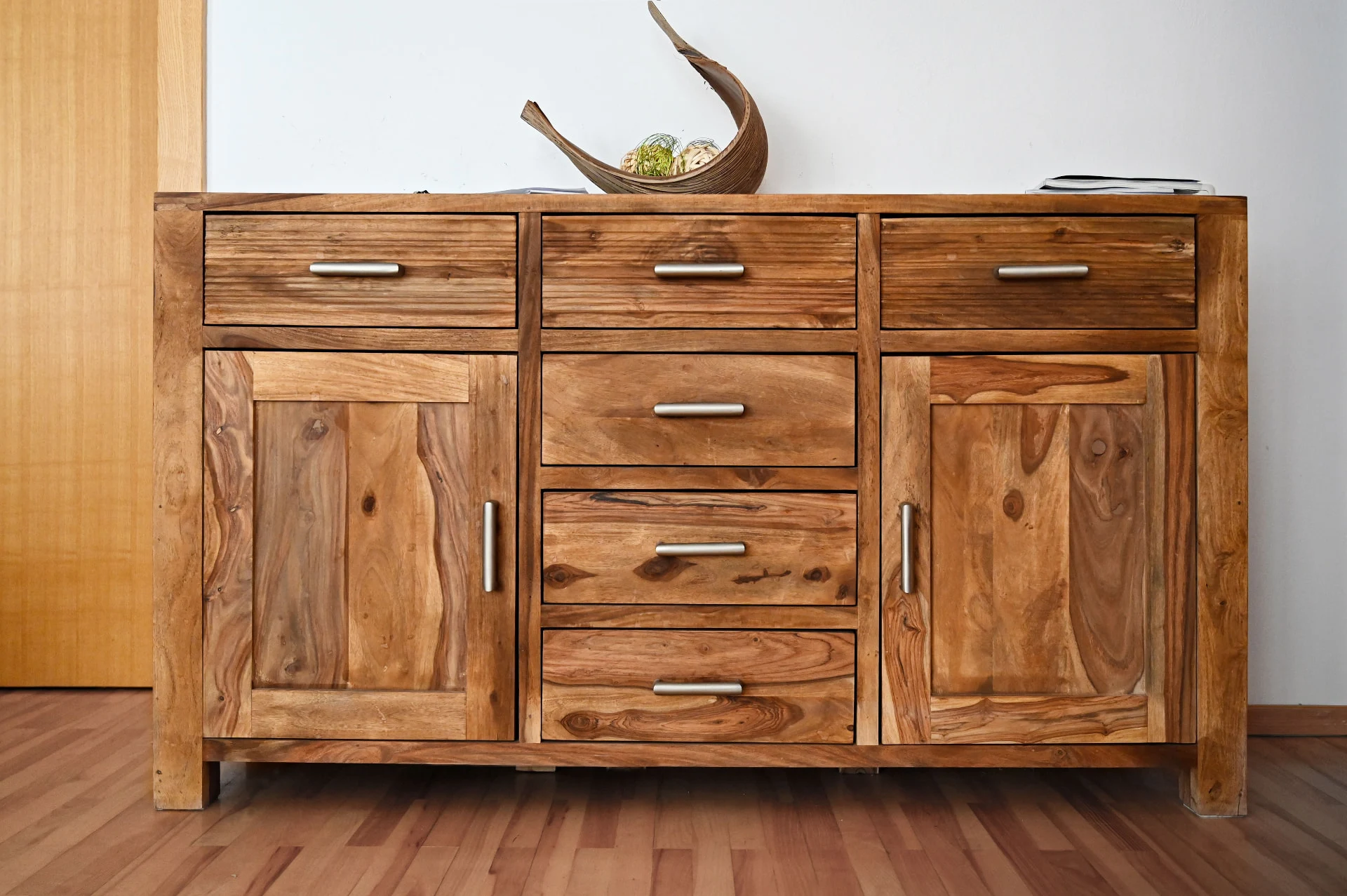 Credenza bassa in legno massiccio con cassetti e maniglie in metallo, in una stanza con pavimento in parquet