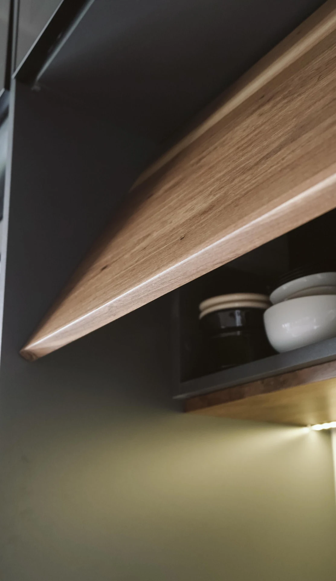 Anta in legno di un pensile da cucina aperta su ciotole in ceramica, illuminata da una luce LED
