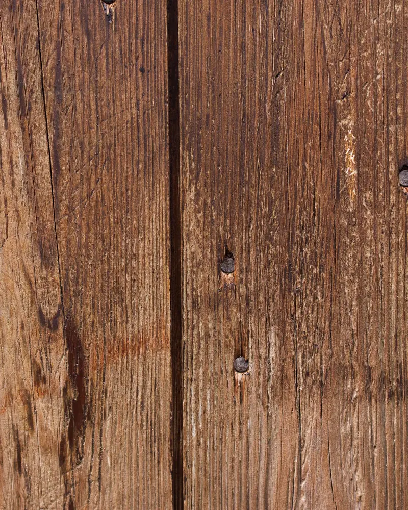 Primo piano di assi verticali di legno antico con venature marcate, fessure e vecchi chiodi in ferro