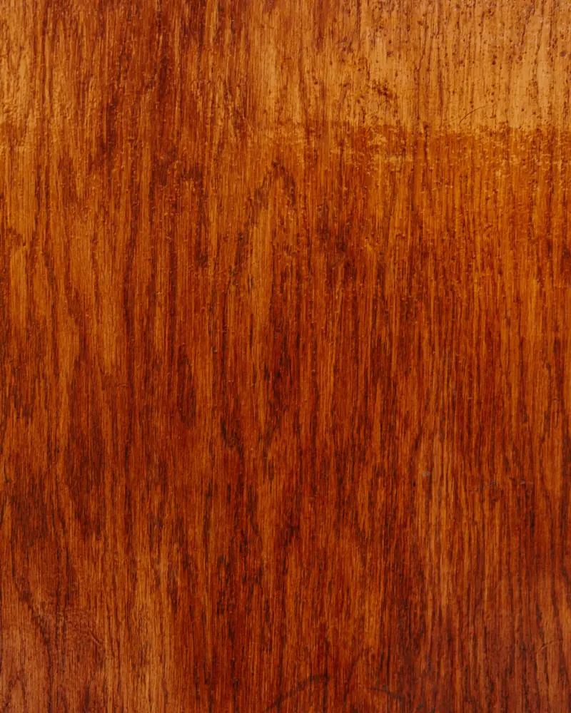 Primo piano di un pannello in legno verniciato in tonalità ambra e noce, con venature naturali a vista