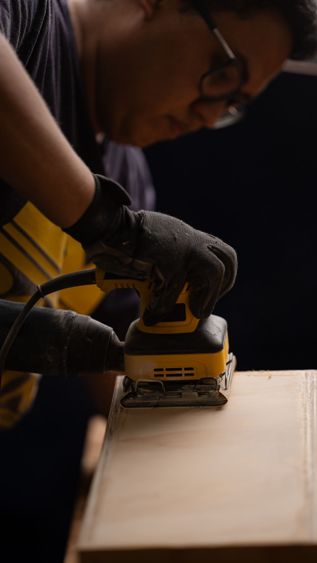 Handwerker mit Handschuhen, der ein Holzbrett mit einer Schleifmaschine schleift