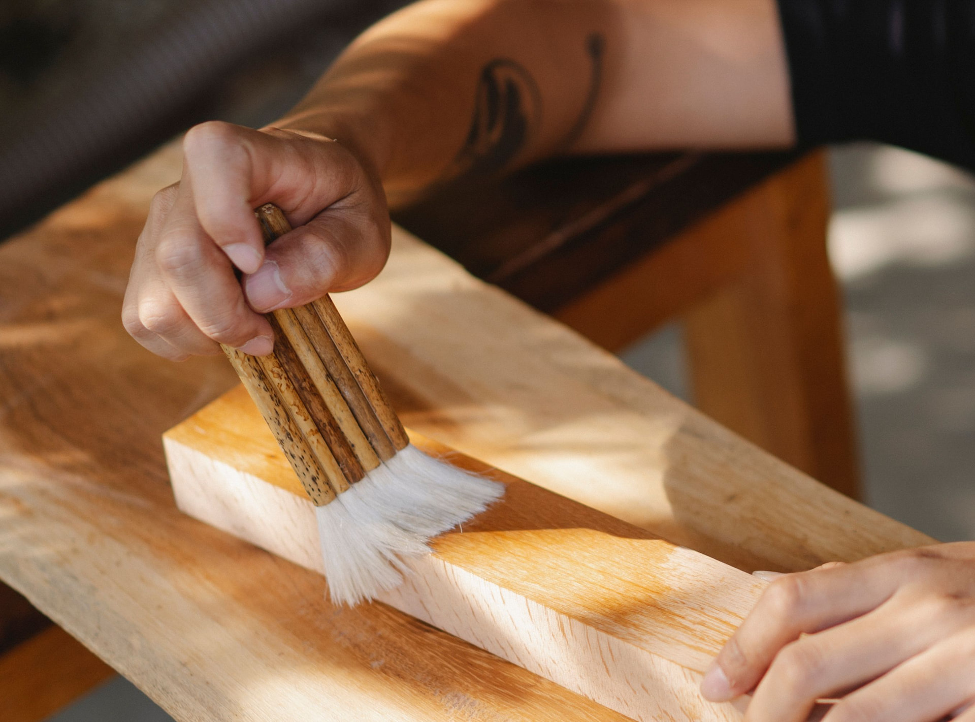 Detailansicht einer Hand, die mit einem Pinsel über ein Holzbrett streicht